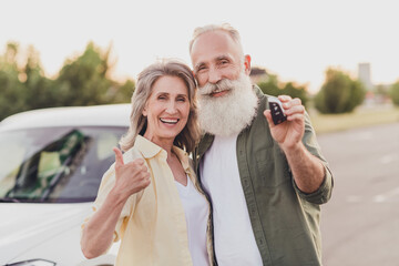 Portrait of elderly retired pensioner cheery couple hugging holding auto key showing thumbup at...