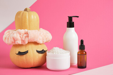 Obraz na płótnie Canvas mock up set of cosmetic containers and pumpkin with headband and false eyelashes on pink background
