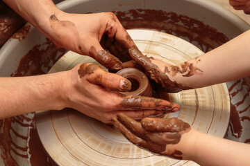 The child moulds from clay a pot on a potter's wheel. Adults help the child to work with clay.