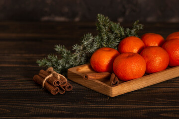 Fototapeta na wymiar Christmas or New Year's still life of tangerines lying on a wooden rectangular plate with spruce branches