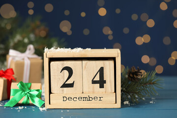 Christmas Eve - December 24. Block calendar, gift boxes and fir tree branch on light blue wooden table