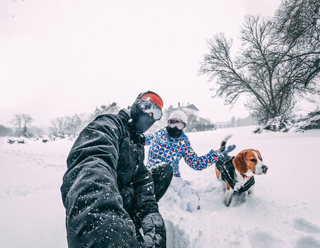 Happy couple with their beagle dog, taking a selfie during a snowstorm, equipped with winter clothes, closeup, vacation concept