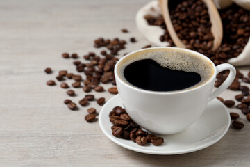 Cup of aromatic coffee and beans on light wooden table. Space for text