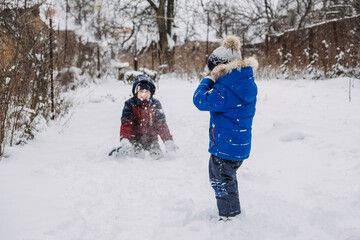 Fototapeta na wymiar Outdoor winter activities for kids. Kids playing in the suburbs, winter backyard gathering. Boys having fun with snow. Selective focus