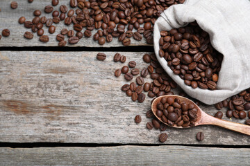 Bag and spoon with roasted coffee beans on wooden table, flat lay. Space for text