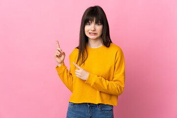 Young Ukrainian woman isolated on pink background frightened and pointing to the side