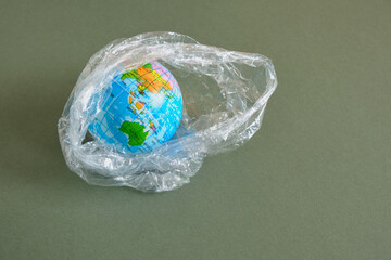 Earth tiy model in polyethylene plastic disposable package, isolated on green background. Concept...
