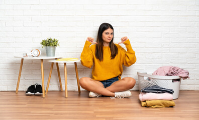 Young woman sitting on the floor at indoors with clothes basket proud and self-satisfied