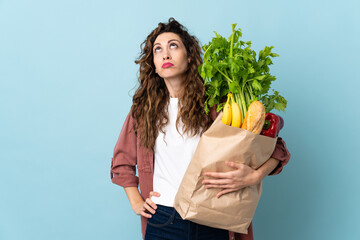 Young woman holding a grocery shopping bag isolated on blue background and looking up