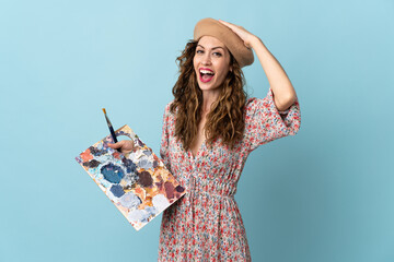 Young artist girl holding a palette isolated on blue background doing surprise gesture while looking to the side