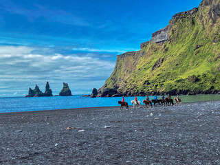 view to the beach with dark sand, horeses riding and impressive rock formation of the Reynisfjara,...