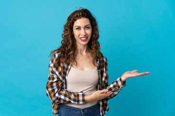 Young caucasian woman isolated on blue background presenting an idea while looking smiling towards