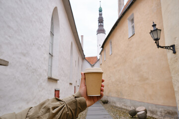 Craft paper cup with coffee in a man's hand. It's time to drink coffee in the city. Disposable paper cup close-up on the background of the city. Empty space for text, layout. Coffee to go concept