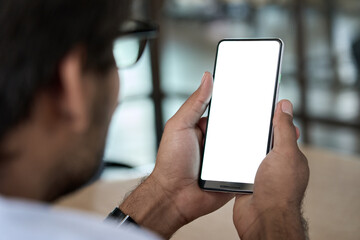 Business man holding phone in hand with white mockup empty blank cellphone screen template using mobile app, smartphone application advertisement, over shoulder closeup view.
