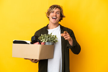 blonde man making a move while picking up a box full of things isolated on yellow background...