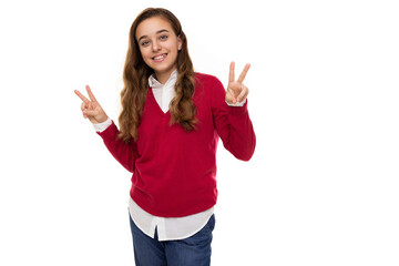 Photo of beautiful cute charming smiling brunette teenage girl with long hair in stylish red sweater and white shirt shows two fingers isolated on white background with free space for text. Peace