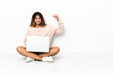 Young woman with a laptop sitting on the floor isolated on white background doing strong gesture