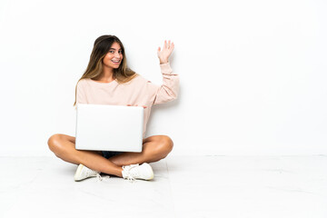 Naklejka premium Young woman with a laptop sitting on the floor isolated on white background extending hands to the side for inviting to come