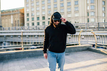 City portrait of handsome hipster guy wearing black blank hoodie with space for your logo or design. Mockup for print