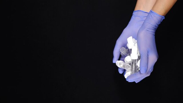 Modern dentistry concept. Empty dental Implant containers in gloved hands shot on black background. Much work and a lot of patients at busy dental office. Vertical footage. Dental implant surgery. 4 k