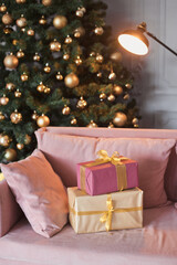 Vertical photo many gift boxes in room interior with a velvet couch, black modern fireplace and gorgeous decorated Christmas tree with in lounge with presents in gold, light green and pink color