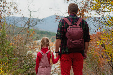 little girl daughter goes with dad on a hike in the autumn forest. back view