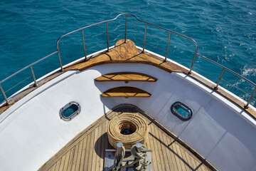 Bow of white yacht on background of blue sea. Bay with thick rope lies on wooden deck. Steel...