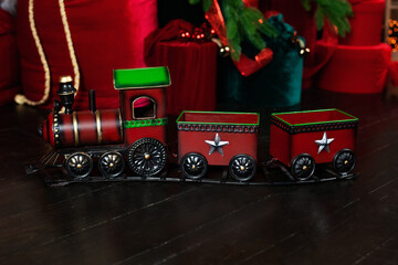 Toy vintage steam locomotive on floor under a decorated Christmas tree and gifts. Xmas toy train on Christmas tree background. Christmas and New year celebration concept. Xmas greeting card with train