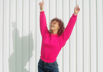 Positive woman with curly pink hair in magenta hoodie posing outdoors. Smiling happy woman concept.