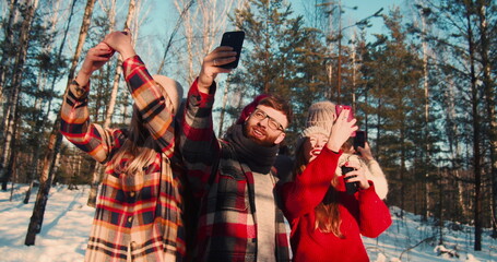 SELFISH CULTURE. Camera moves around happy multiethnic friends taking selfies at sunny snowy winter forest slow motion.