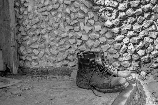 old dirty worn men's military motorcycle boots stand on the doorstep of the house. monochrome, black and white photo