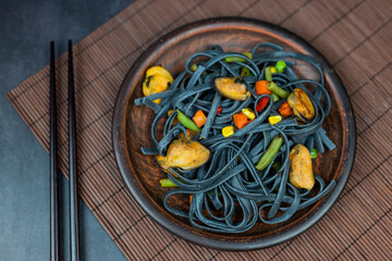 dish noodles black with vegetables and mussels asian food with chopsticks