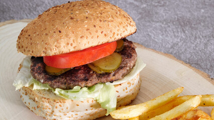 Close-up of tasty hamburger with french fries tomato and cucumber pickle on a natural wooden tray