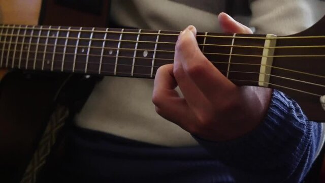 close-up of a musician's hands playing various notes on an electro-acoustic guitar in his room
