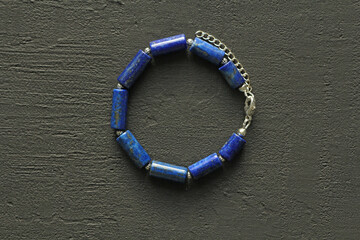 Blue natural lapis lazuli Bracelet made of natural stones lies on a black modern concrete background. Blue stone lapis lazuli. Handmade jewelry from natural stones. Handmade bracelets