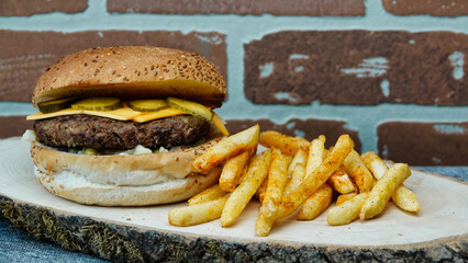 Close-up of  tasty hamburger with cheddar cheese french fries, american salad and cucumber pickle on a natural wooden tray