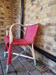 Old red rattan chair outside against a brick wall with blue feet and brick floor with black down pipe