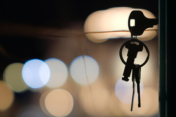 The keys with house keyring in the door keyhole with blurred night lights background, selective focus