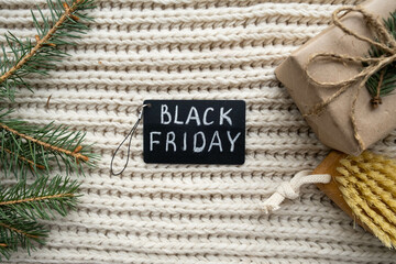 Black Friday big sale promotional sign with handmade gift, fir branches and massage brush on cozy soft background. Christmas Spa and Winter Skin Care Concept. Flat lay, copy space
