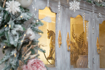 Golden rocking horse toy behind the glass of cupboard, decorated with snowy fir branches and icy roses, snowflakes and icycles