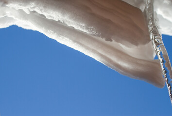 Snow hanging from the roof on blue sky background