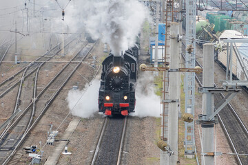 A steam locomotive driving through the railway station, releasing smoke and steam