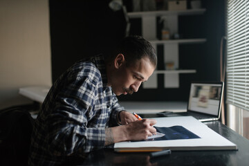 Male artist drawing in sketchbook at desk in artists studio