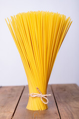 A vertical bunch and a bunch of raw spaghetti tied with string. Bundle on a wooden background....
