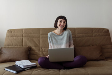 Female student studying at home- she is sitting on a couch and using laptop