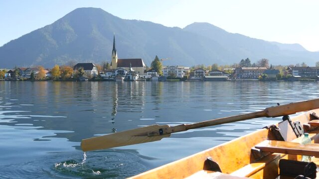 A peaceful picture a wooden boat with an oar floats on beautiful mountain lake Tegernsee against backdrop of Alpine mountains and the picturesque container of the church. Ferryman ferries people