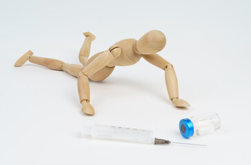 The wooden man crawls towards the syringe and injection. Isolated on white background.