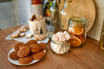 Merry Christmas and Happy New Year! On the table is a plate of cookies, jars of marshmallows and candied oranges. Table decoration for the holiday.