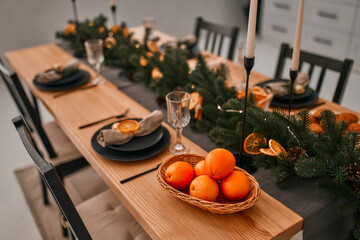 Merry Christmas and Happy New Year! Preparing for a festive dinner. Table setting and decoration with candles, spruce branches and dried orange wedges.