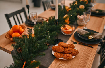 Fototapeta na wymiar Merry Christmas and Happy New Year! Preparing for a festive dinner. Table setting and decoration with candles, spruce branches and dried orange wedges.
